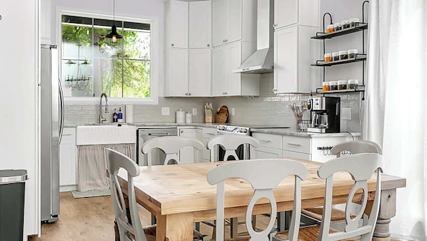 Une cuisine moderne avec des meubles blancs, une table à manger en bois et une cuisinière intégrée.