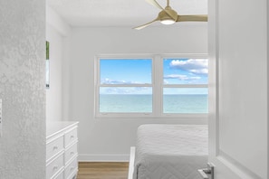 A bedroom with a view of the sea, a ceiling fan, and a white dresser.