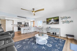 A modern living room with a gray sofa, a white coffee table, and a blue rug with sea creature patterns. - Oceanfront Condo w/ Balcony + Rocket Launch Views (Satellite Beach)