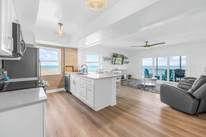 A modern kitchen with a central island, a dining area with a view, and a living room with a gray sofa. - Oceanfront Condo w/ Balcony + Rocket Launch Views (Satellite Beach)