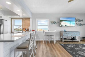 A modern kitchen with a large island, white cabinetry, and a view of the beach. - Oceanfront condo w/ balcony & rocket launch views (Satellite Beach)