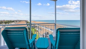 Un balcon avec des chaises turquoise et une table donnant sur une plage et sur le paysage urbain.