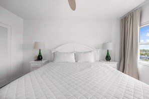 Ein Hotelzimmer mit einem großen Bett, einem weißen Kopfteil, zwei Nachttischen mit Lampen und einem Vorhangfenster.