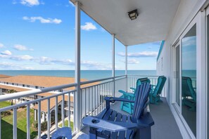 Un balcon offrant une vue sur l’océan, avec des fauteuils Adirondack bleus et une balustrade blanche.