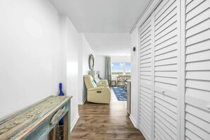 Un couloir doté d’un plancher en bois, d’un canapé beige, d’une petite table et offrant une vue sur l’extérieur.