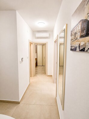 A hallway with a light-colored floor, white walls, and a ceiling with a recessed light fixture.