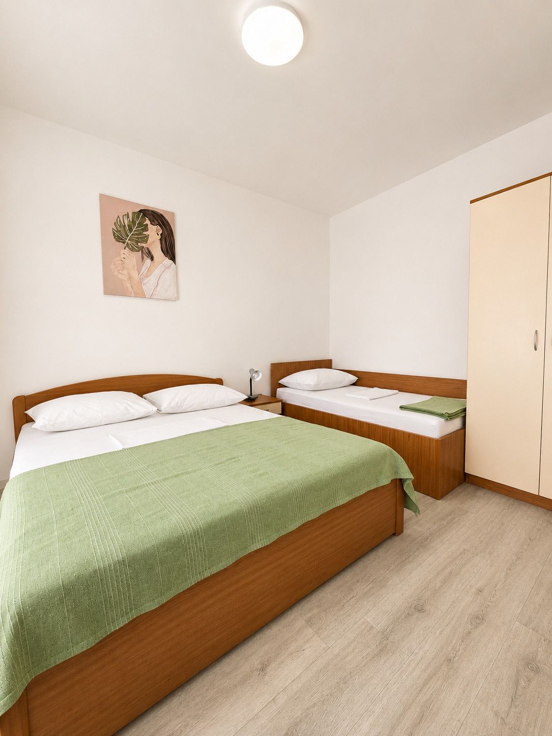 Un dormitorio con dos camas, una colcha verde, una lámpara de noche y un armario.