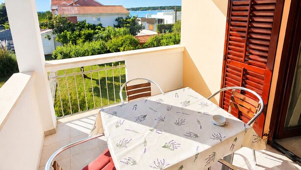 Ein Balkon mit Tisch und Stühlen, Blick auf ein Gebäude und einer Brüstung.