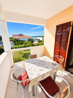A balcony with a table and chairs, a view of a building, and a railing. - Apartment Olinda (Zaton)