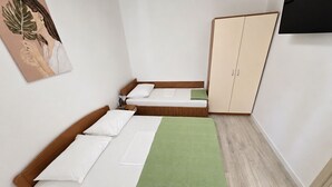 Ein Zimmer mit zwei Einzelbetten, einem Kleiderschrank, einer grünen Decke und einem Bild an der Wand.