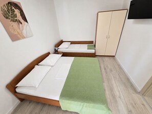 A room with two single beds, a wardrobe, a green blanket, and a painting on the wall.