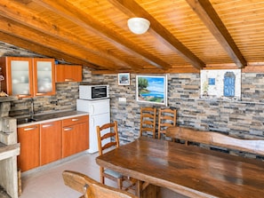 A compact kitchen with wooden cabinets, a stone backsplash, and a dining area with a wooden table and chairs. - Apartment Marcela (Zaton)