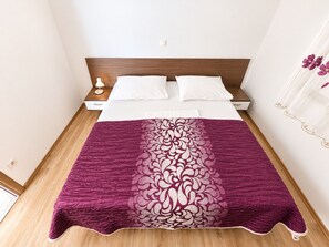 A neatly made bed with a white duvet and pillows, a wooden headboard, and a purple patterned throw blanket. - Apartment Marcela (Zaton)