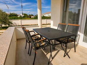 An outdoor patio with a table and chairs, a view of the neighborhood, and a building with a white facade.