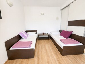 A room with two beds, a small table, and a wall-mounted light fixture. - Apartment Aora (Zaton)