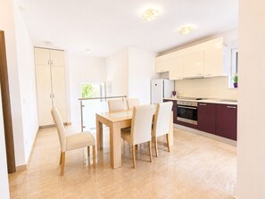 A modern kitchen with a dining area, featuring a wooden table and chairs, a refrigerator, and a stove.