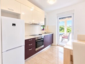 A modern kitchen with a refrigerator, stove, and sink, leading to a balcony with a table and chairs. - Apartment Aora (Zaton)