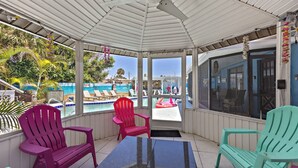 A covered outdoor area with a pool, red and green chairs, and a table.