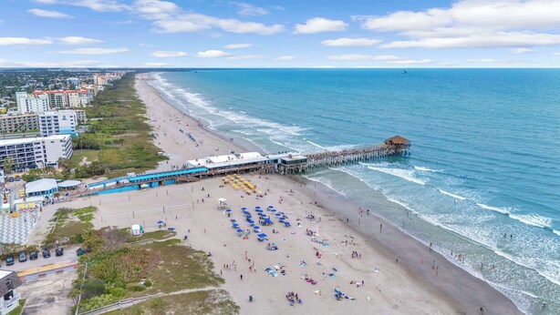 A beach with a pier, beach umbrellas, and a hotel in the background.