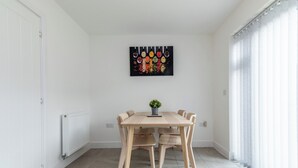 Ein Essbereich mit Holztisch und Stühlen, einer Topfpflanze und einem farbenfrohen Kunstwerk an der Wand.