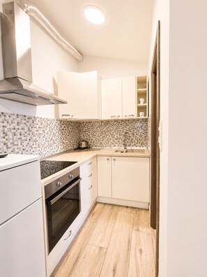 Une cuisine de taille réduite avec des meubles blancs, un pare-feu en carrelage et un plancher en bois.