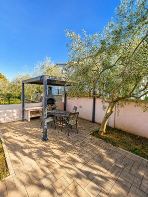 Een buitenpatio met een barbecue, zithoek en een pergola.