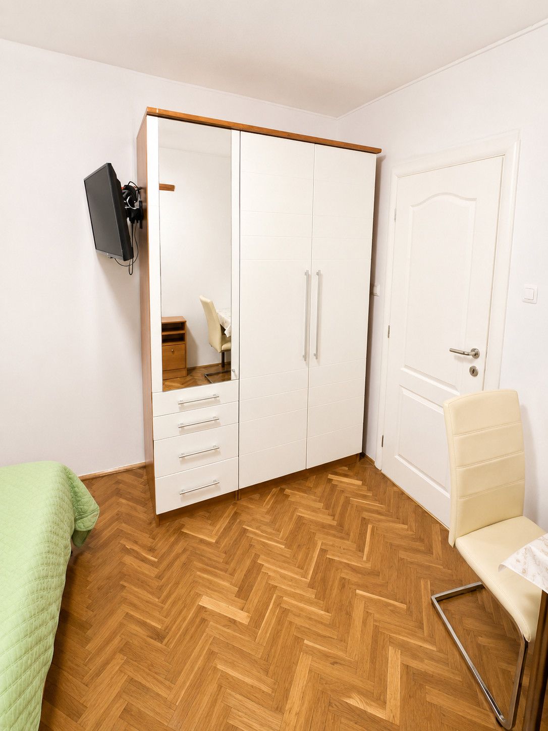 Una habitación con armario, una silla, una cama y un televisor montado en la pared.