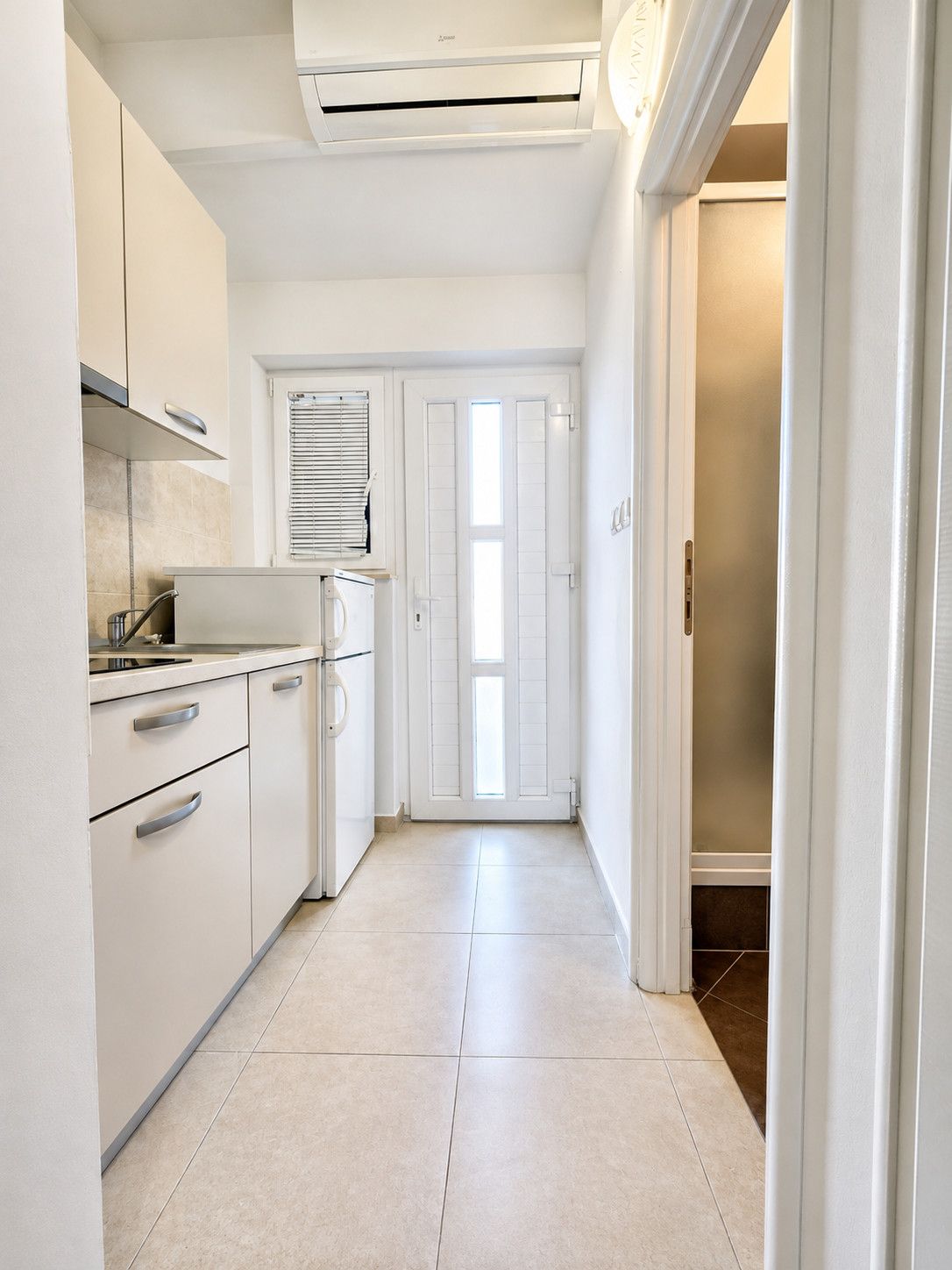 A kitchen with white cabinets, a built-in oven, and a window with blinds.