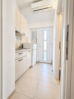 A narrow kitchen with white cabinets, a built-in oven, and an air conditioning unit. - Studio apartment Vita (Zaton)