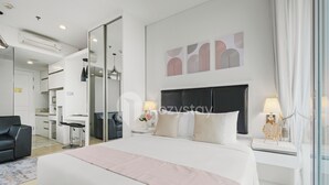 A modern hotel room with a large bed, a desk, a chair, and a view of the city. - Bona by Kozystay - Ciumbuleuit (Bandung)