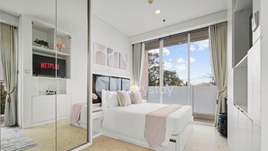 A modern bedroom with a large bed, a TV mounted on a wall, and a balcony with curtains. - Bona by Kozystay - Ciumbuleuit (Bandung)