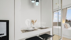 A modern hotel room with a white desk, two black barstools, a large mirror, and a view of the outdoors through a sliding glass door. - Bona by Kozystay - Ciumbuleuit (Bandung)