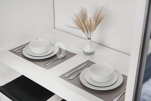 A neatly set dining table with white plates, bowls, and cutlery on a textured placemat.