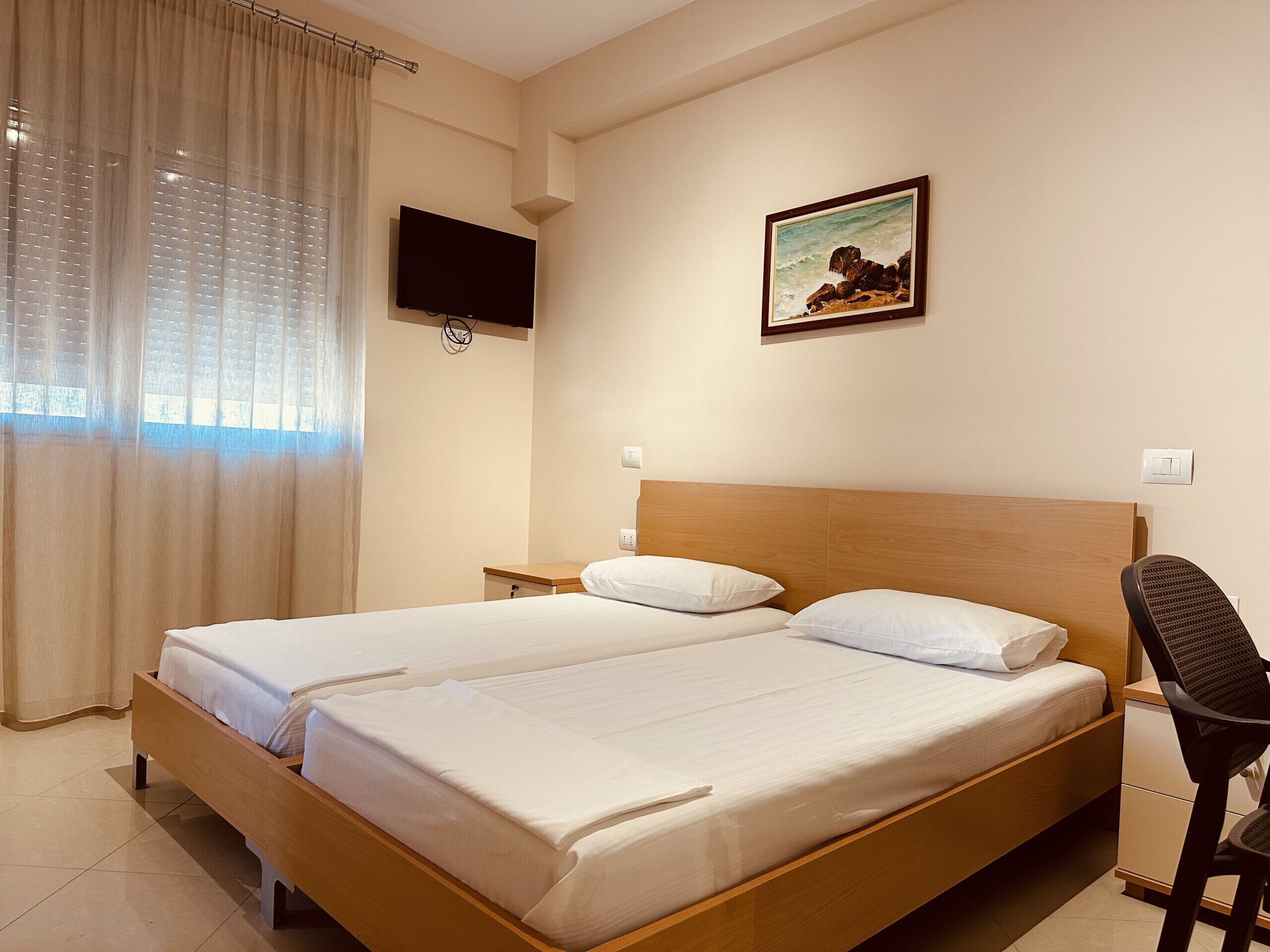 A hotel room with a double bed, a TV mounted on the wall, a painting above the bed, and a chair.