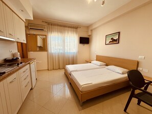 A hotel room with a bed, a desk, a chair, a TV, and a window with curtains.