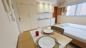 A hotel room with a bed, a dining table set with plates and cutlery, a red candle, and a kitchen area with cabinets and a sink. - Thoma's K Studios - Double Studio (Vlorë)