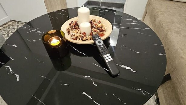 A round black table with a remote control, a candle, and a decorative item.