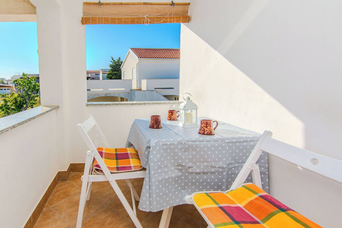 A balcony with a table and chairs, a view of buildings, and a clear sky.