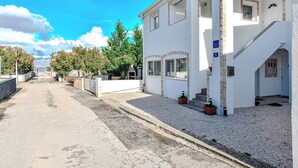 A two-story white building with a gravel driveway and a clear blue sky. - Apartments Ladika (Vir)
