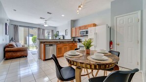 A modern kitchen with a dining area, including a round table with chairs, a sofa, and a view to the outside. - Relaxing 3BR townhome w/ resort access (Kissimmee)