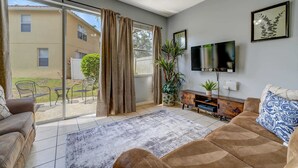 A living room with a sofa, TV, and sliding glass doors leading to a patio. - Relaxing 3BR townhome w/ resort access (Kissimmee)