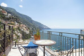 A balcony with a table, chairs, and a potted plant overlooking a coastal town and the sea. - Sea Soul Positano (Positano)