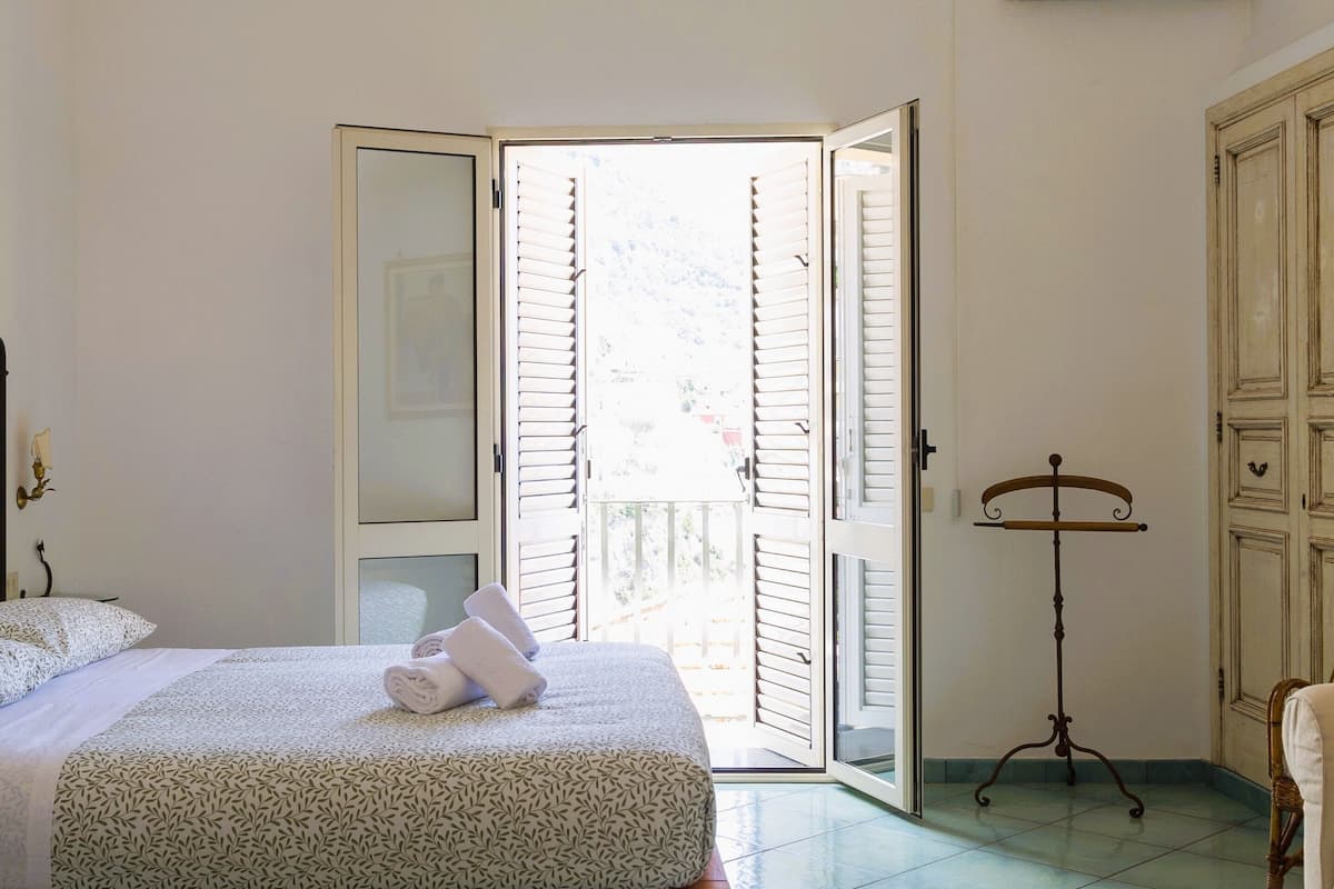 A bedroom with a bed, a chair, a wardrobe, and a music stand.