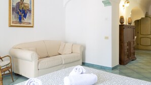 A room with a beige sofa, a patterned rug, a rolled white towel, a wooden cabinet, and a painting on the wall. - Sea Soul Positano (Positano)