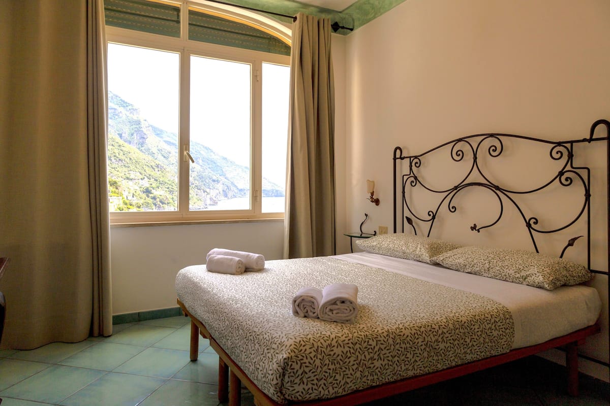A bedroom with a bed, curtains, a window with a mountain view, and a bedside table with a lamp.