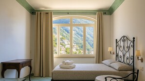 A bedroom with a bed, a nightstand, a window with curtains, and a view of a mountainous landscape. - Sea Soul Positano (Positano)
