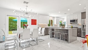 Una cocina moderna con una isla central, taburetes de bar y un comedor con sillas blancas.