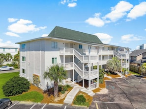 A multi-story building with a central staircase, a parking lot, and surrounding greenery. - Island Retreat Walk to Beaches & Harbor (Destin)