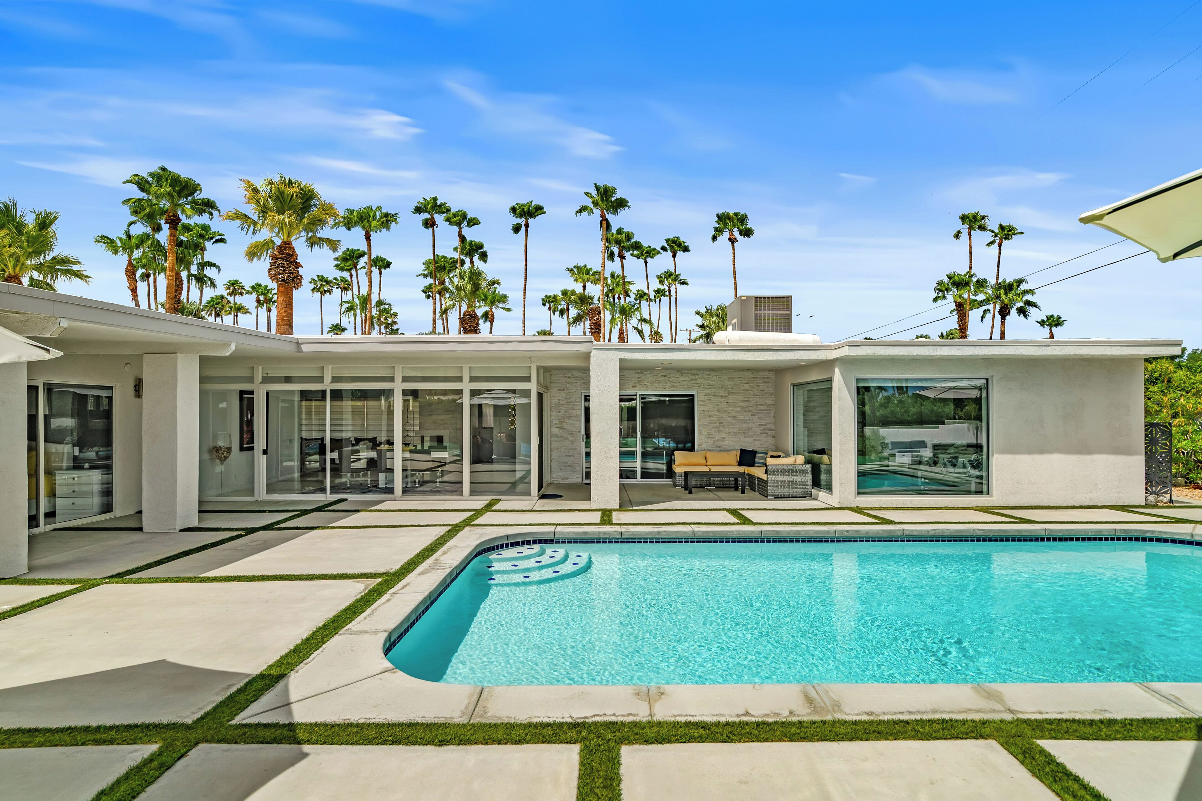 A modern house with a swimming pool, glass doors, and palm trees.