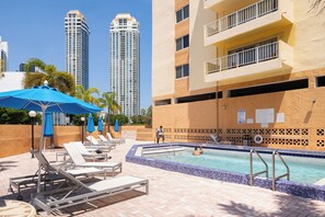 A pool area with lounge chairs, a pool, and high-rise buildings in the background.